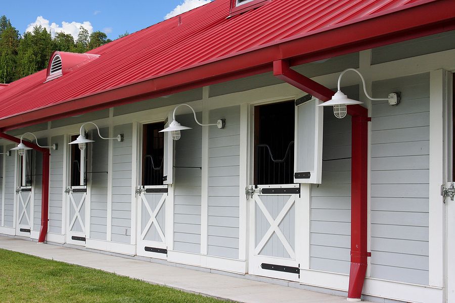 red metal roof and gutters on a gray and white horse stable