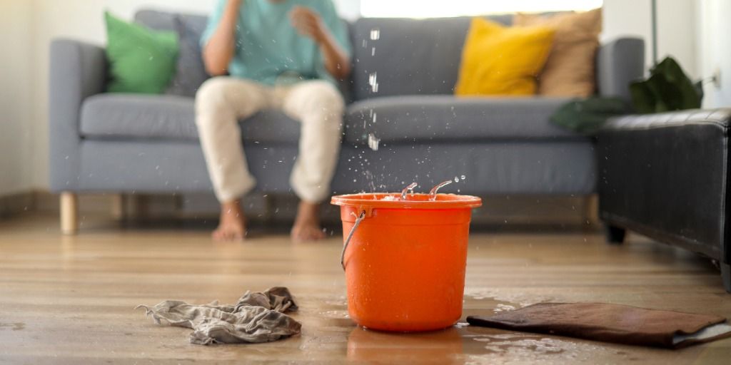 Orange bucket collecting ceiling leak water with towels on floor for emergency roof leak cleanup