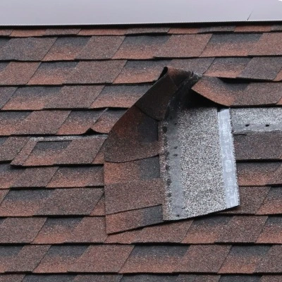 Damaged asphalt shingles with missing sections exposing roof deck requiring emergency repair