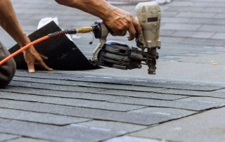Close-up of roofing contractor's hands installing asphalt shingles with nail gun during roof replacement