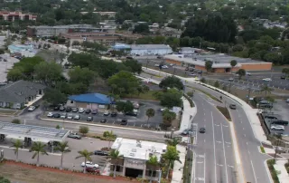 An aerial view of a Florida commercial district featuring various buildings with flat TPO roofs, sloped asphalt shingles, and large retail centers requiring commercial roof maintenance.