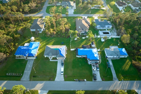Aerial neighborhood view showing multiple Florida homes with blue emergency roof tarps after hurricane damage, demonstrating widespread storm-related roof repairs requiring building permit compliance and insurance claims