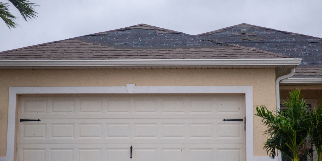 Storm-damaged asphalt shingle roof on a Florida home showing missing shingles and exposed underlayment beneath overcast skies