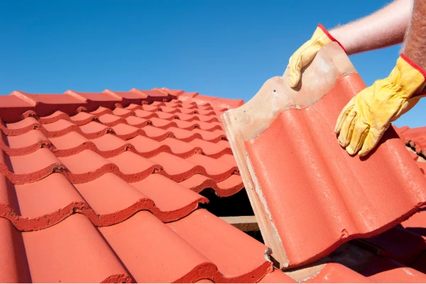 Roofing contractor replacing a damaged clay tile on a residential roof during a tile roof repair service