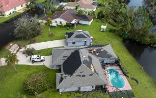 Aerial view of homes with severe hurricane storm damage showing missing shingles and exposed roof decking.