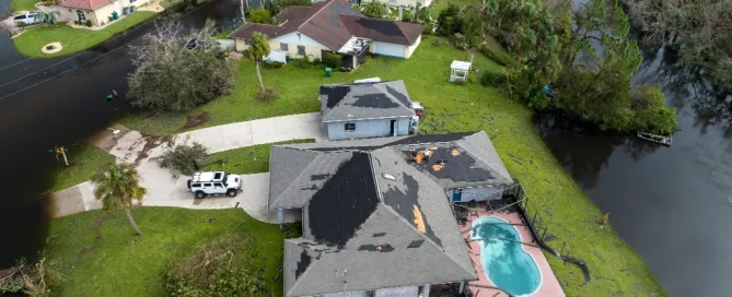 Aerial view of homes with severe hurricane storm damage showing missing shingles and exposed roof decking.