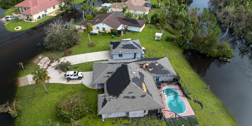 Aerial view of homes with severe hurricane storm damage showing missing shingles and exposed roof decking.