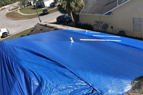 A blue tarp covering a storm-damaged residential roof in a Florida neighborhood, awaiting emergency roof repair service.