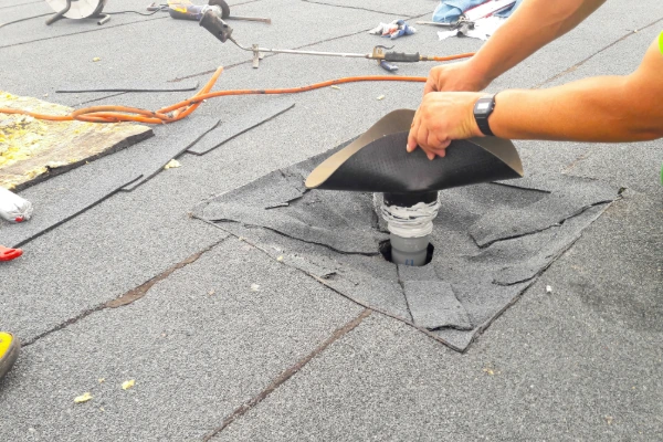 Roofer sealing a pipe boot flashing during flat roof repair and maintenance.